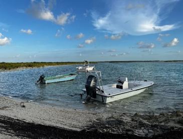 Small boats in shallow water, under a blue sky dotted with clouds.