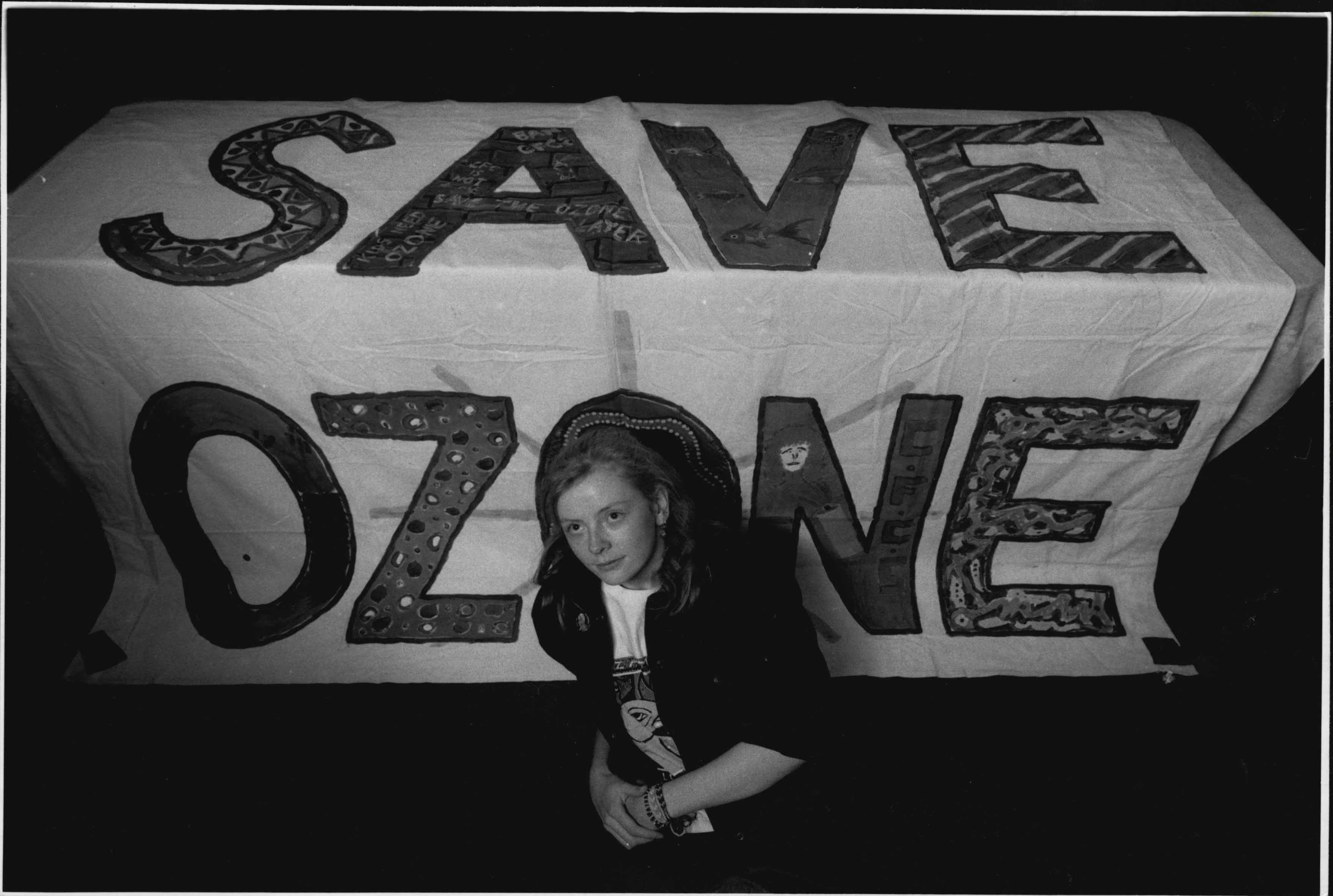 A person sitting in front of a "save ozone" sign.