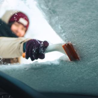Woman cleans windshield with ice scraper
