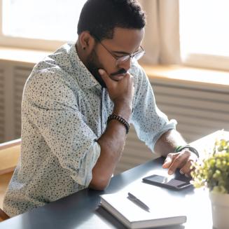 Man sitting at a desk looking thoughtfully at a cell phone