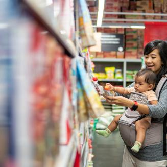 A mom shopping with her baby in a drugstore aisle, as the baby grabs at a product container.