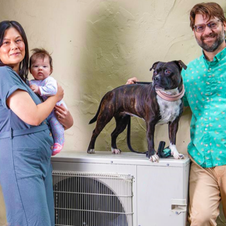 The Grow family standing next to their heat pump with their dog on top of it