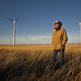 Pete Ferrell standing in a grassy field in front of wind turbines.