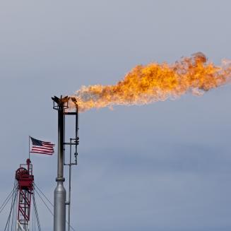 Oil and gas flare in front of an overcast sky with a U.S. flag next to it.