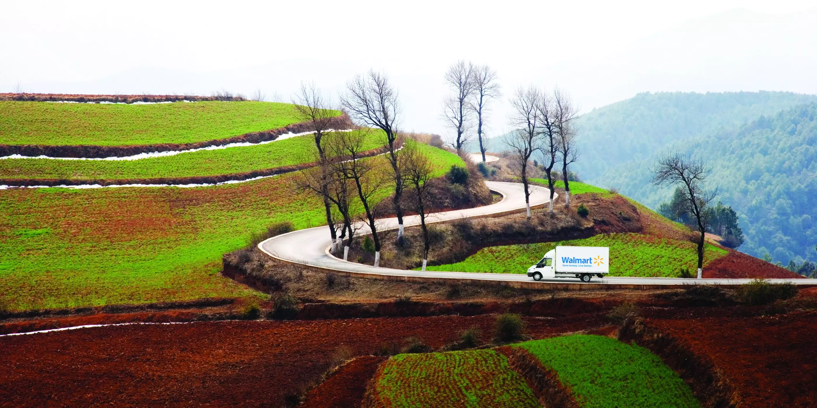 Walmart truck drives up a curved road in a scenic landscape.