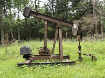 An orphaned oil well in a grassy overgrown field.