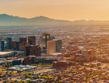 Panoramic view of Arizona city skyline with mountains in background and yellow sun at right